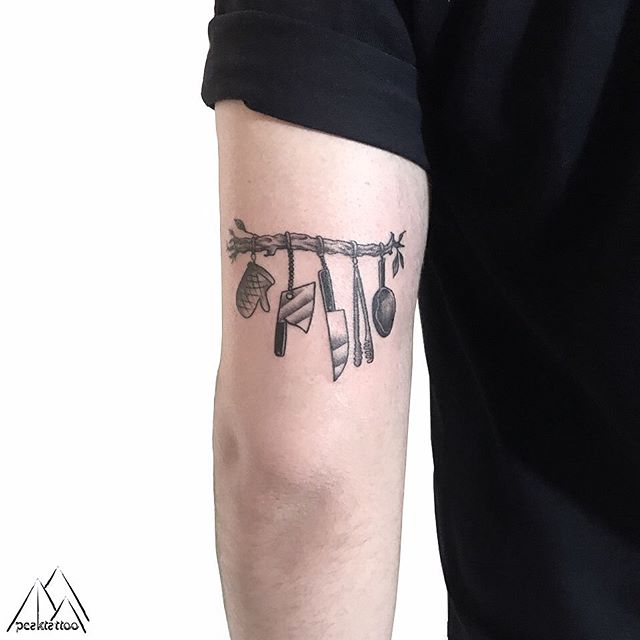 Black tattoo of kitchen tools, which are hanging on the branch, on the left hand
