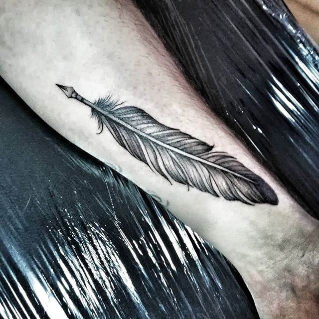 Black tattoo of a quill on the right leg
