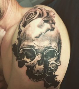 Black tattoo of a skull and rose on the left shoulder
