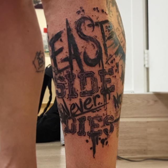 Lettering tattoo of a "east side never dies" on the left calf