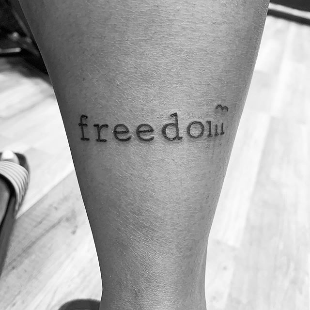 Lettering tattoo of a "freedom" on the right calf