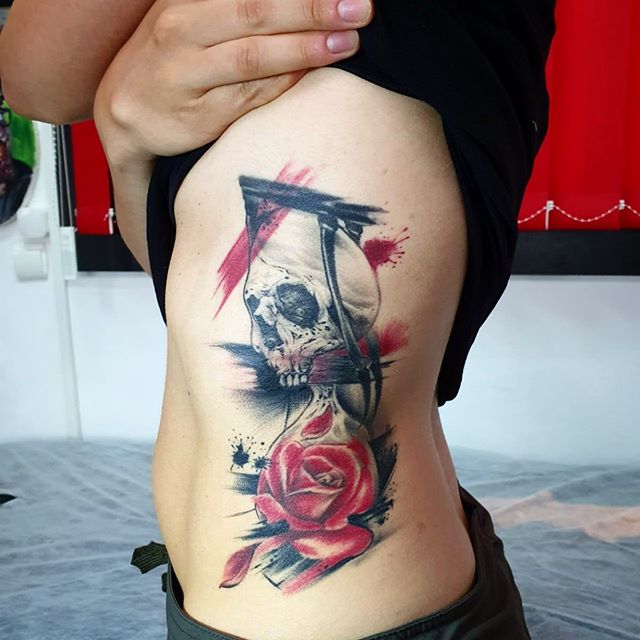 Trash polka tattoo of a skull with a red rose on the left side of ribs