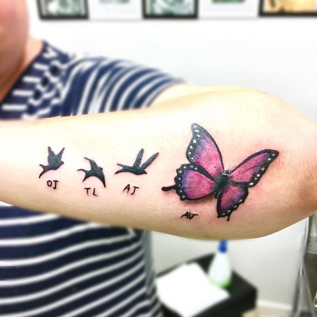 Forearm tattoo of black birds and a color butterfly
