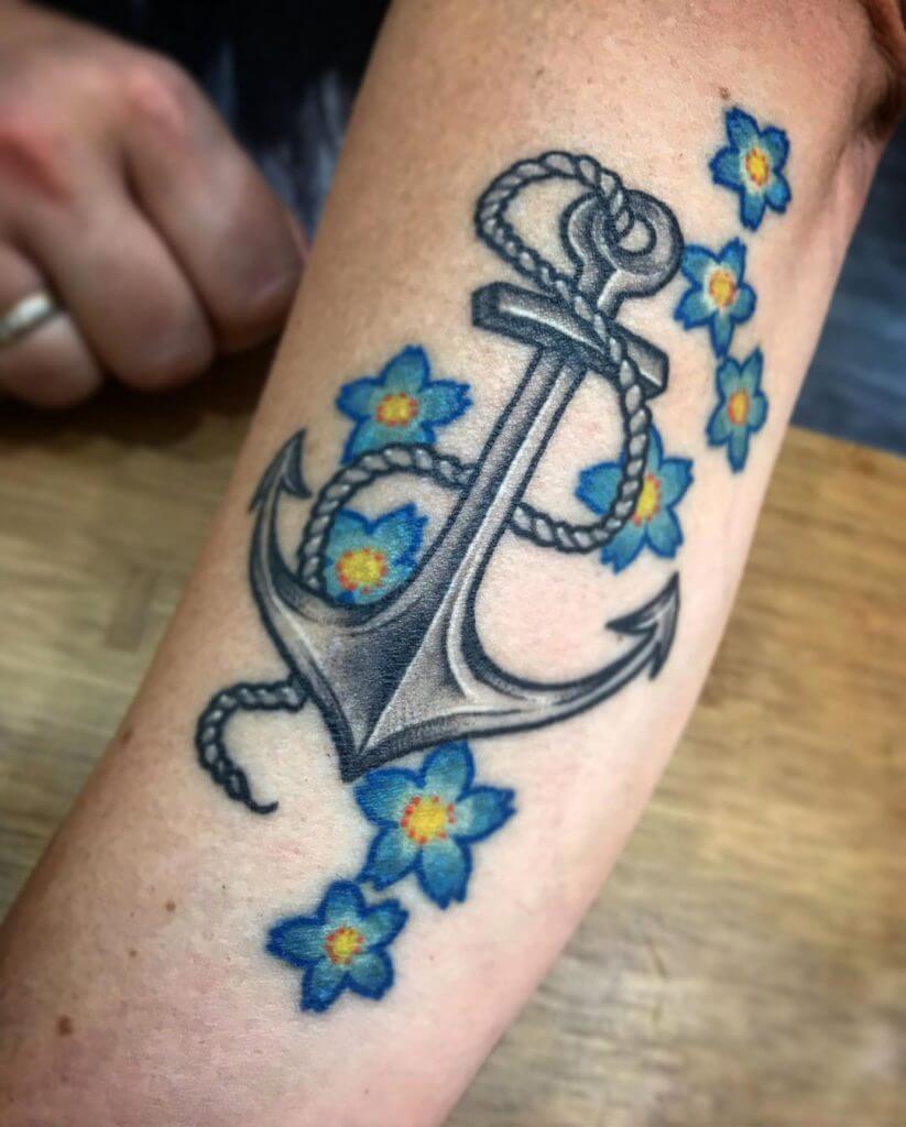 Anchor tattoo with blue flowers on the left forearm