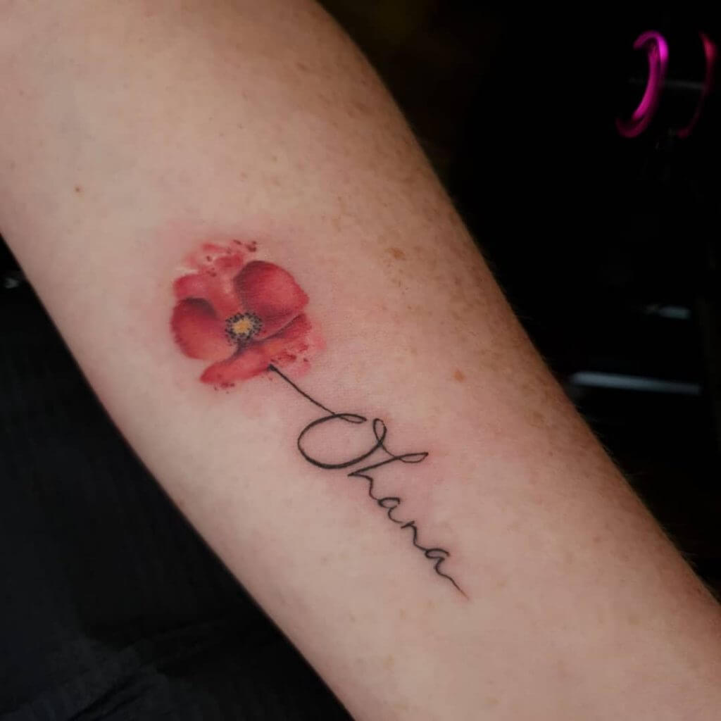 Color Female tattoo of a wild poppy and letters on the left forearm