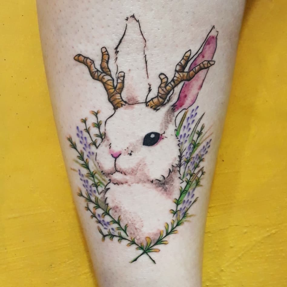 Color tattoo of a bunny with antlers and a flowers on the forearm