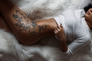 Beautiful woman with a black and grey tattoo of a flower on her leg and ribs