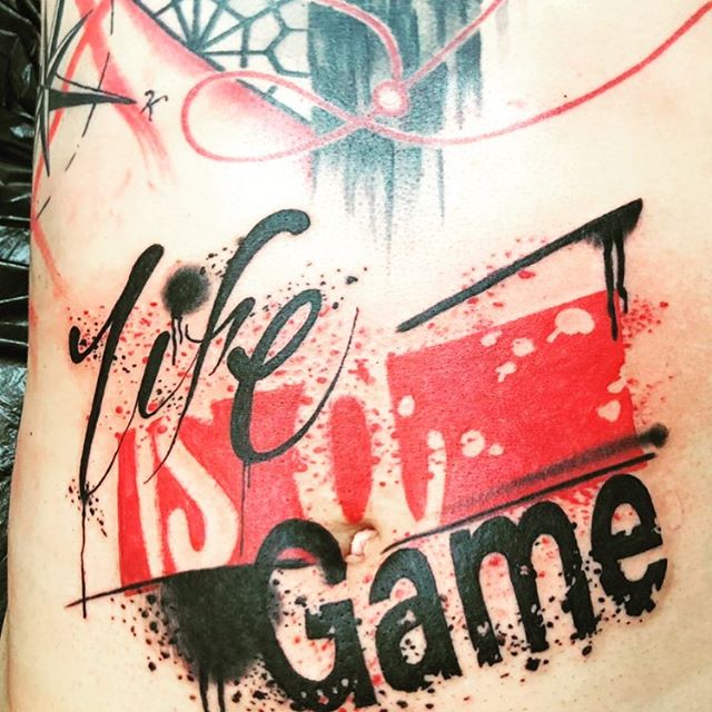 Trash polka tattoo of the text "Life is a Game" on a belly