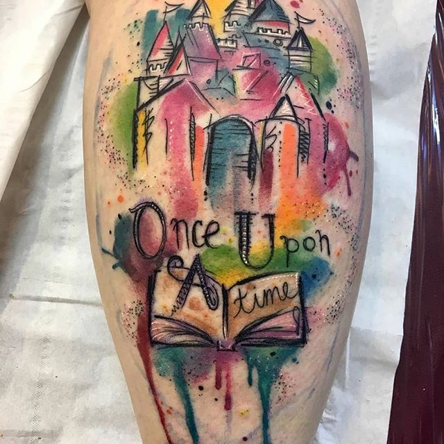 Watercolor tattoo of an old town with a book and the text "Once Upon a time" on the calf