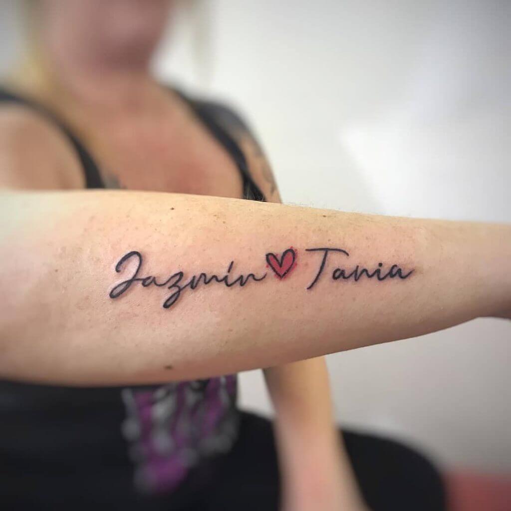 Lettering black tattoo for women of "Jazmin ❤️ Tania" written on the right forearm