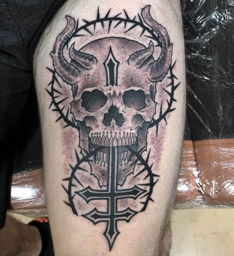 Black neotraditional tattoo of a devil skull with a reversed cross and a barbed wire on left thigh