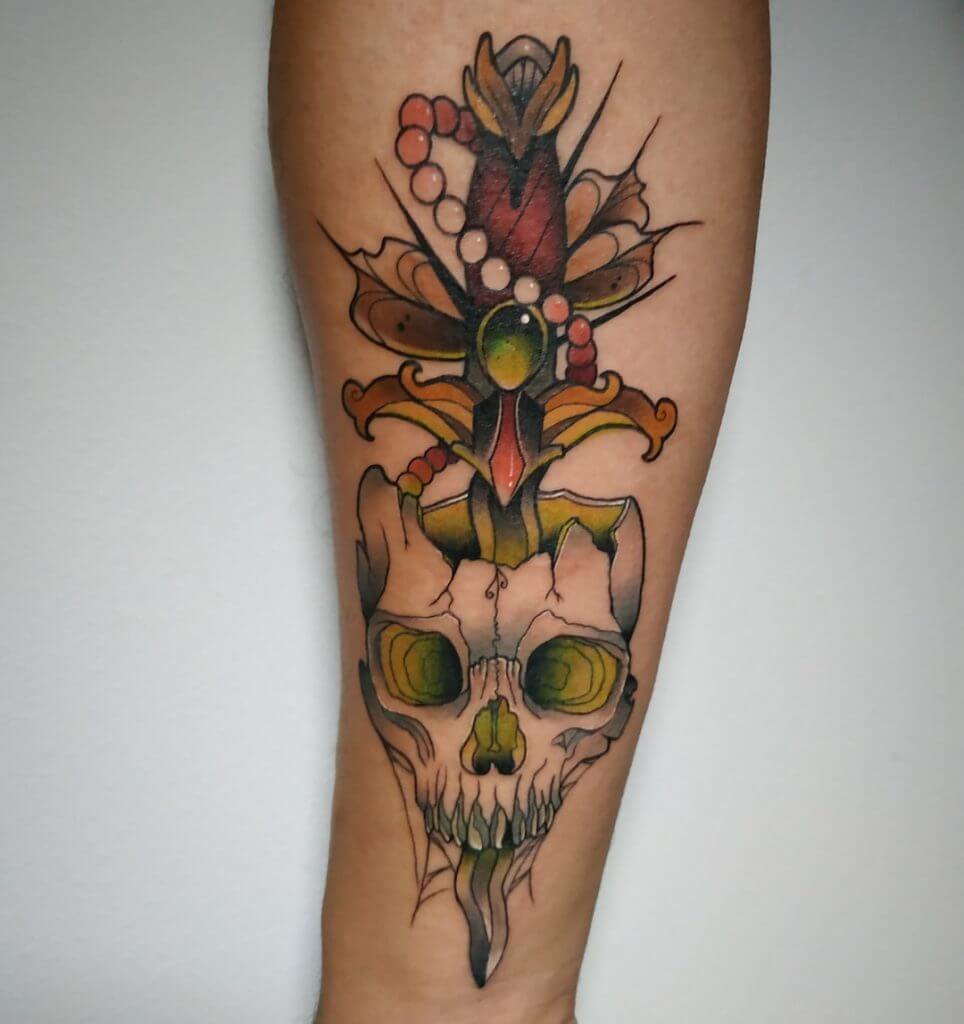Color neotraditional tattoo of a skull with dagger on the forearm