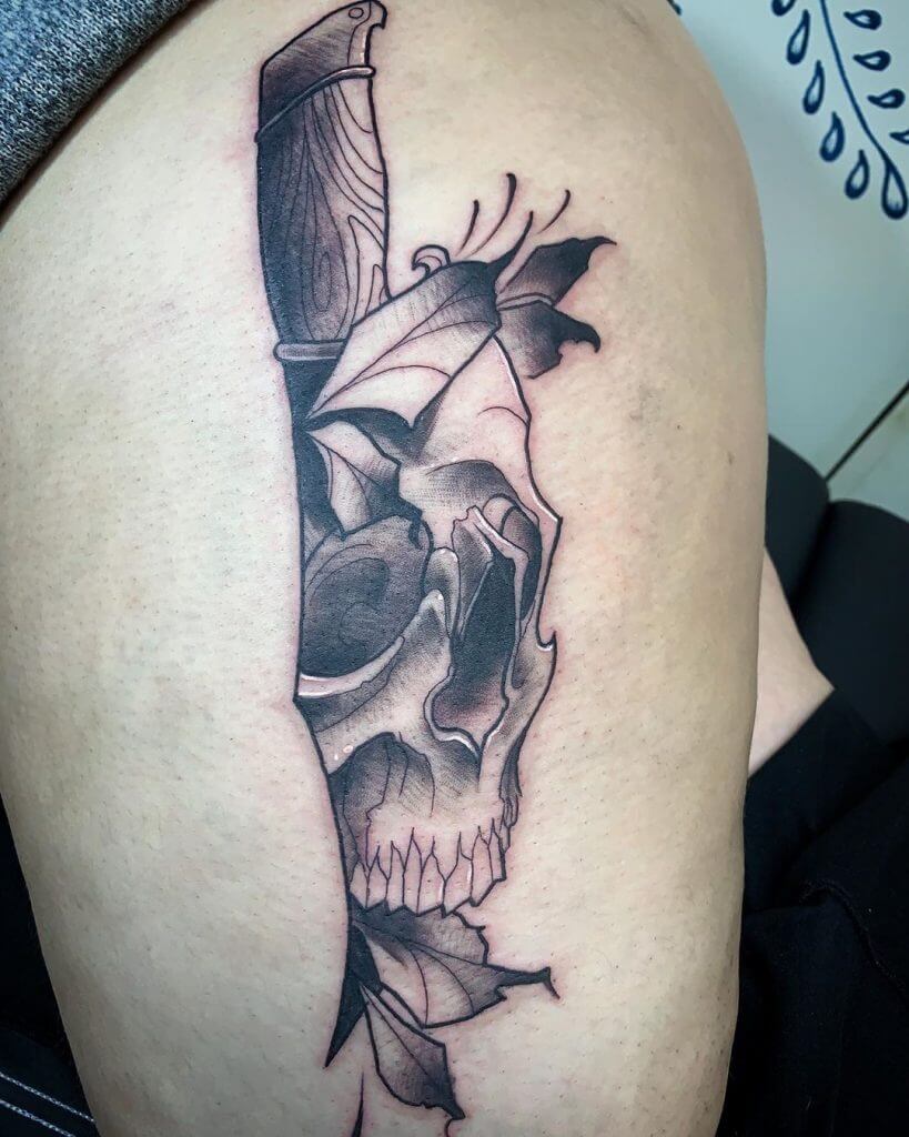 Black neotraditional tattoo with a skull, leaves and a knife on the left thigh
