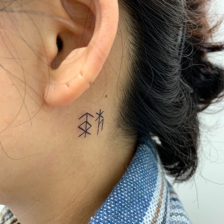 Small black abstract tattoo behind the left ear