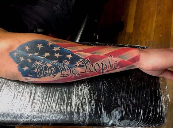 Forearm We the People tattoo with a flag